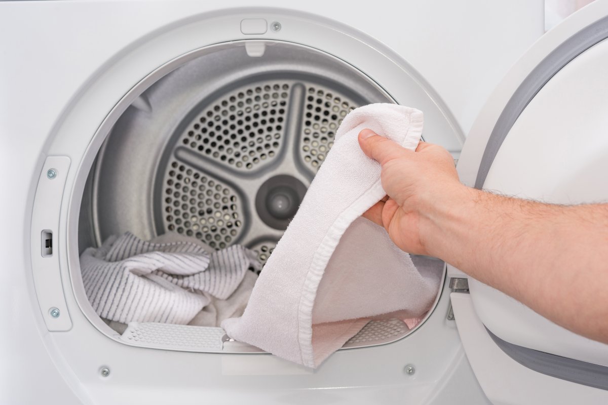 Hand putting a white towel into a dryer