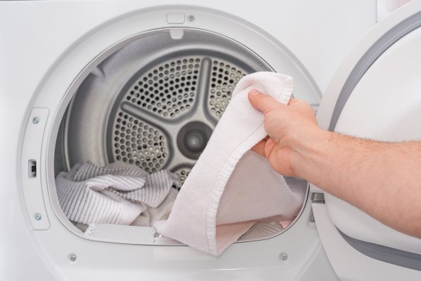 Hand putting a white towel into a dryer