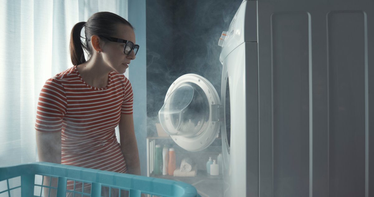 Upset woman staring at her broken washing machine, the room is full of smoke