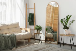 Stylish room interior with leaning floor mirror and sheer window treatments letting the sunlight in.