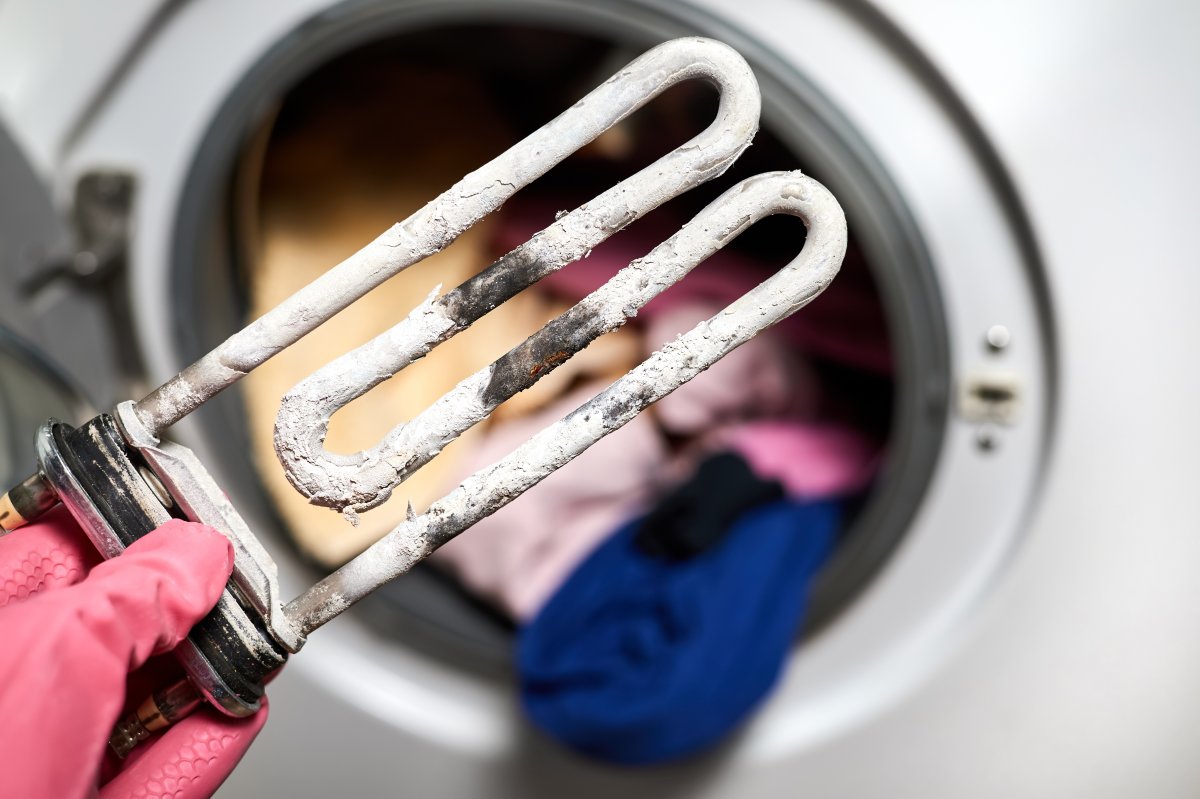 A man holds in his hand a burnt-out heating element of a washing machine against the background of a washing machine