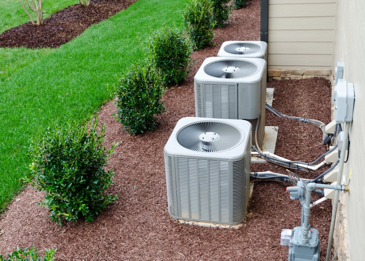 Three AC units connected to the residential house that are surrounded by brown mulch.