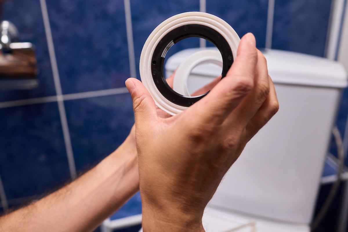 Person holds a toilet ring in front of a toilet in a blue-tiled bathroo.