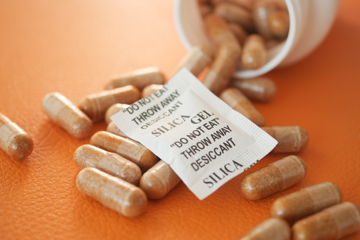 Silica gel packet rests next to spilled capsules on orange background.