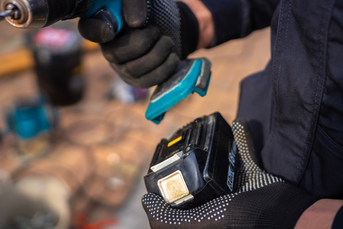 A person wearing work gloves removes a battery pack from an old power drill. 