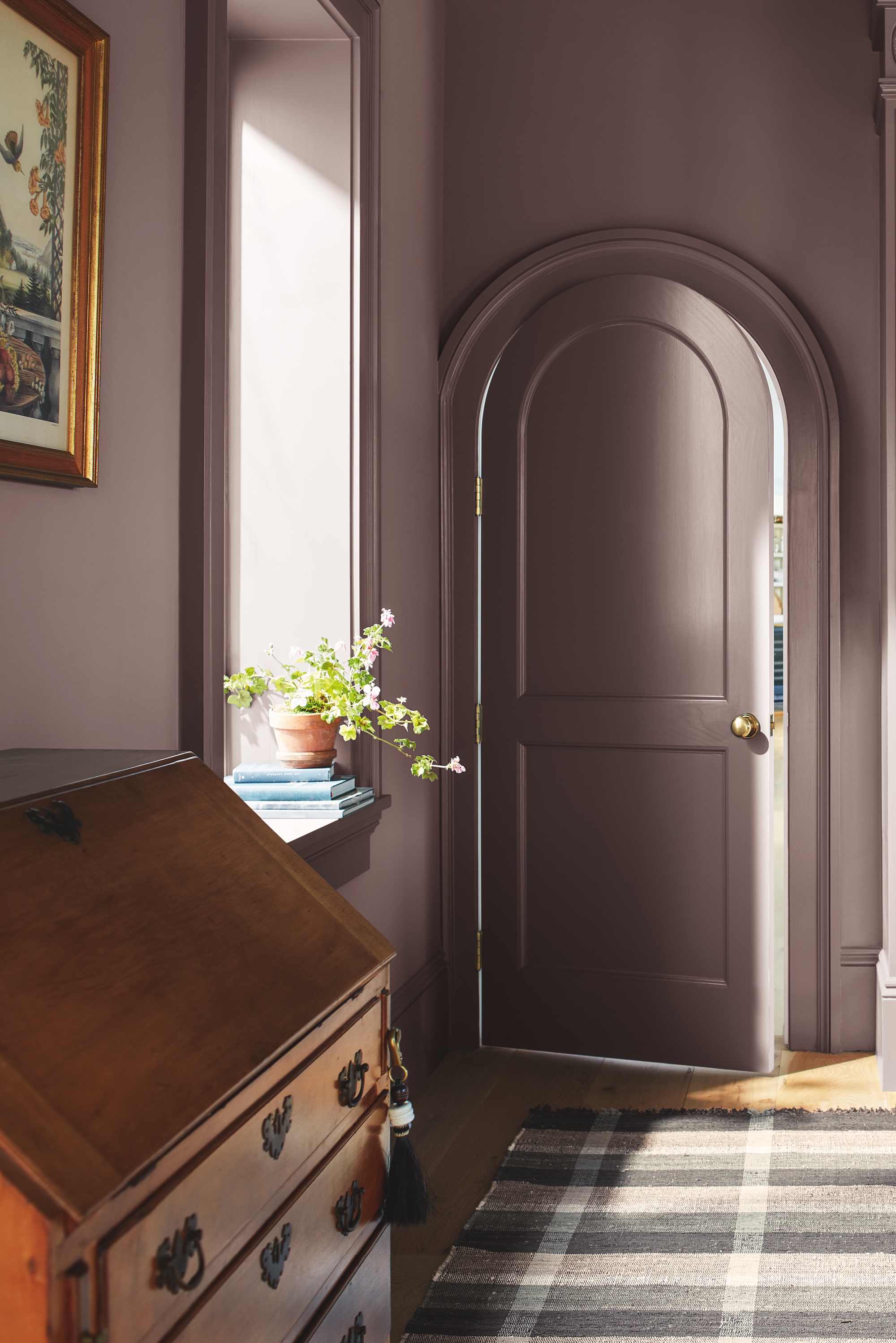 Benjamin Moore's Cinnamon Slate color-drenching an office with ornate trim work around a rounded door and a large window.