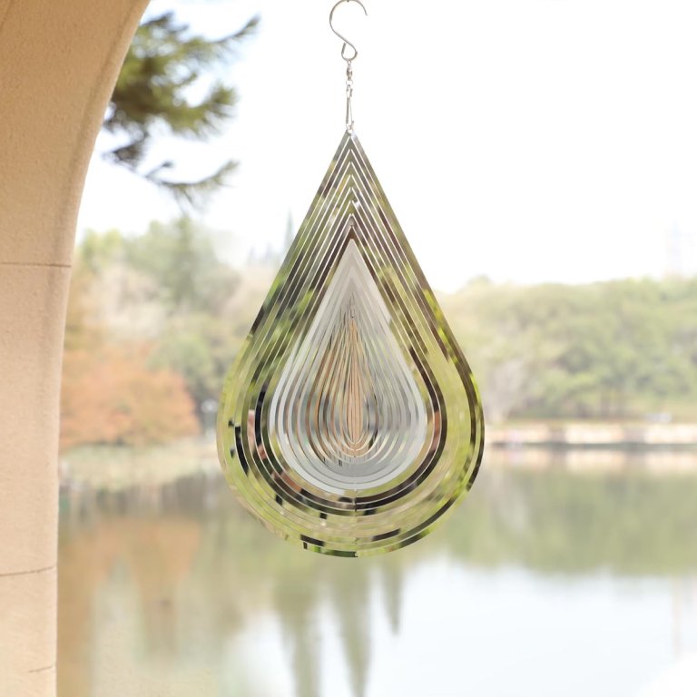 The CosyCorner Stainless Steel Water Drop Wind Spinner hanging in front of a lake