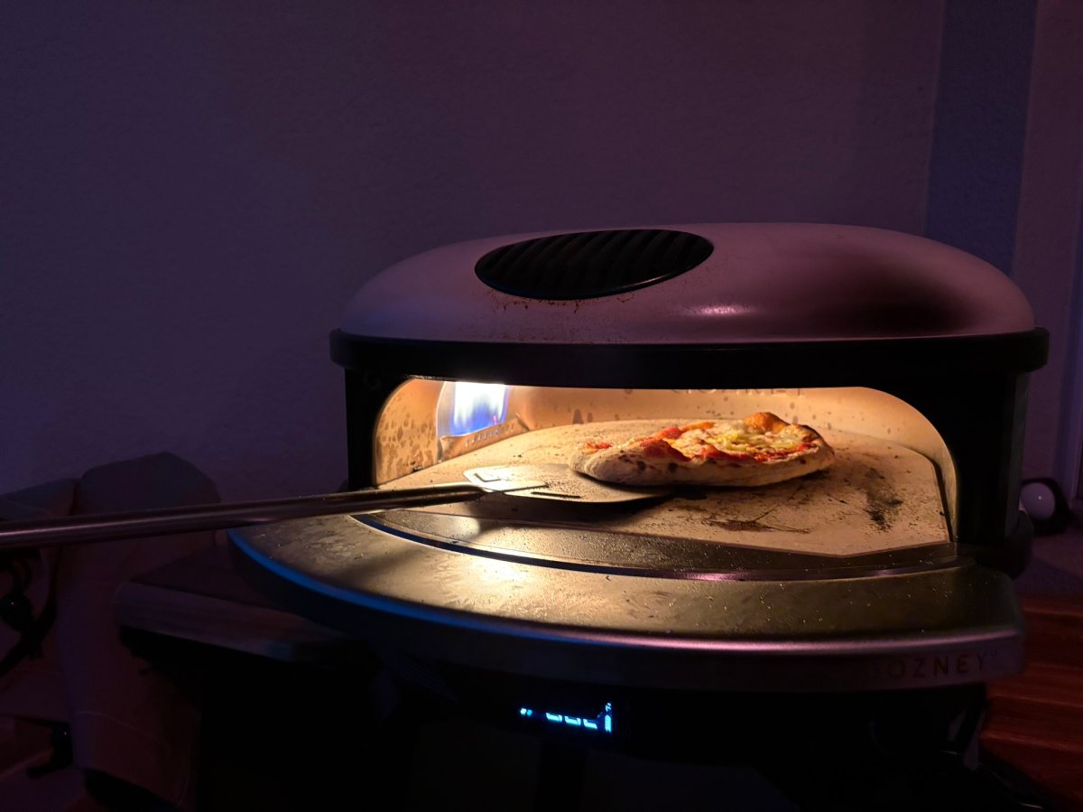 A product tester using a pizza peel to pull a cooked pizza out of a Gozney pizza oven