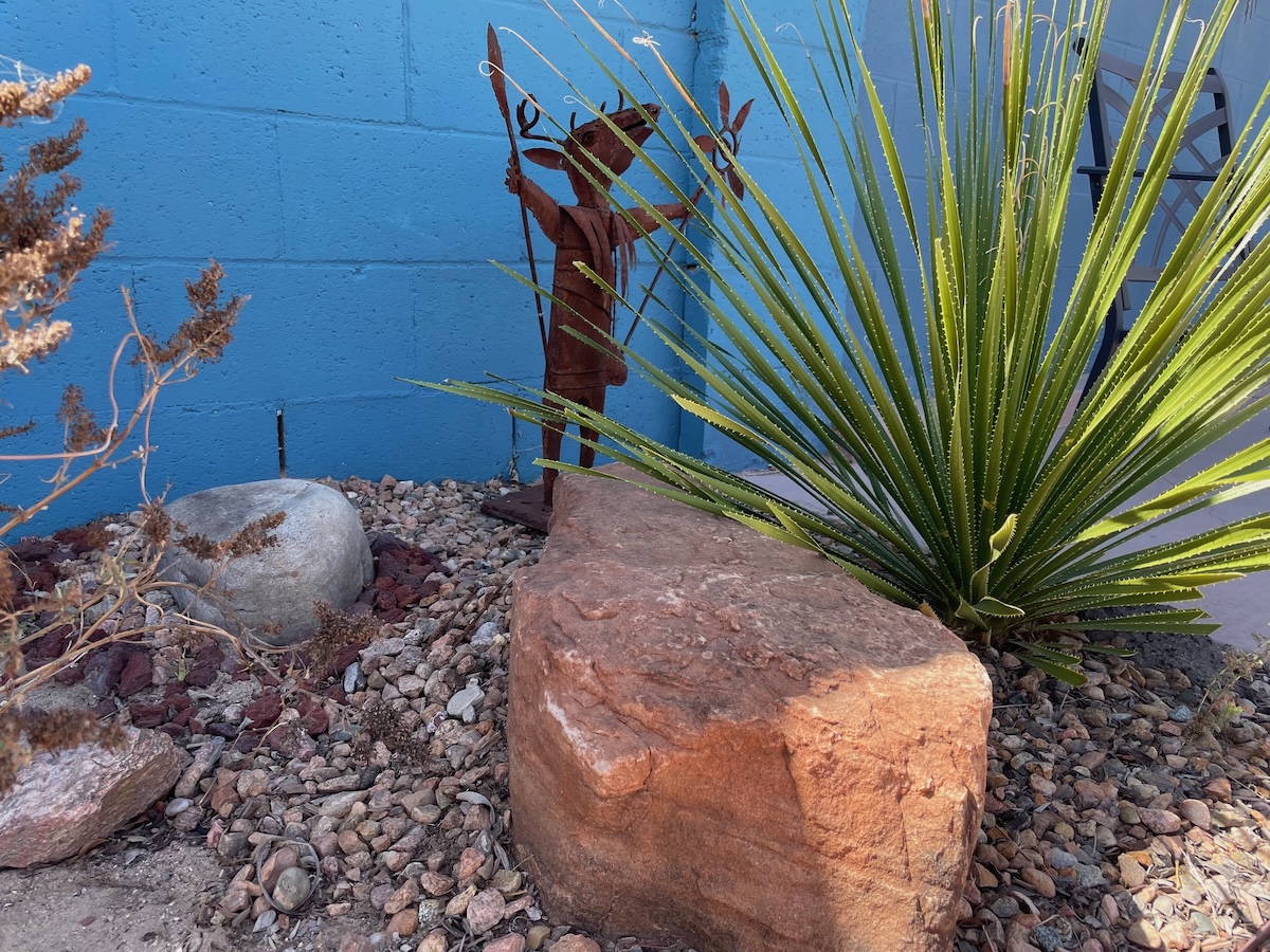 A vignette in a home landscape featuring big rocks, plants, and garden art.