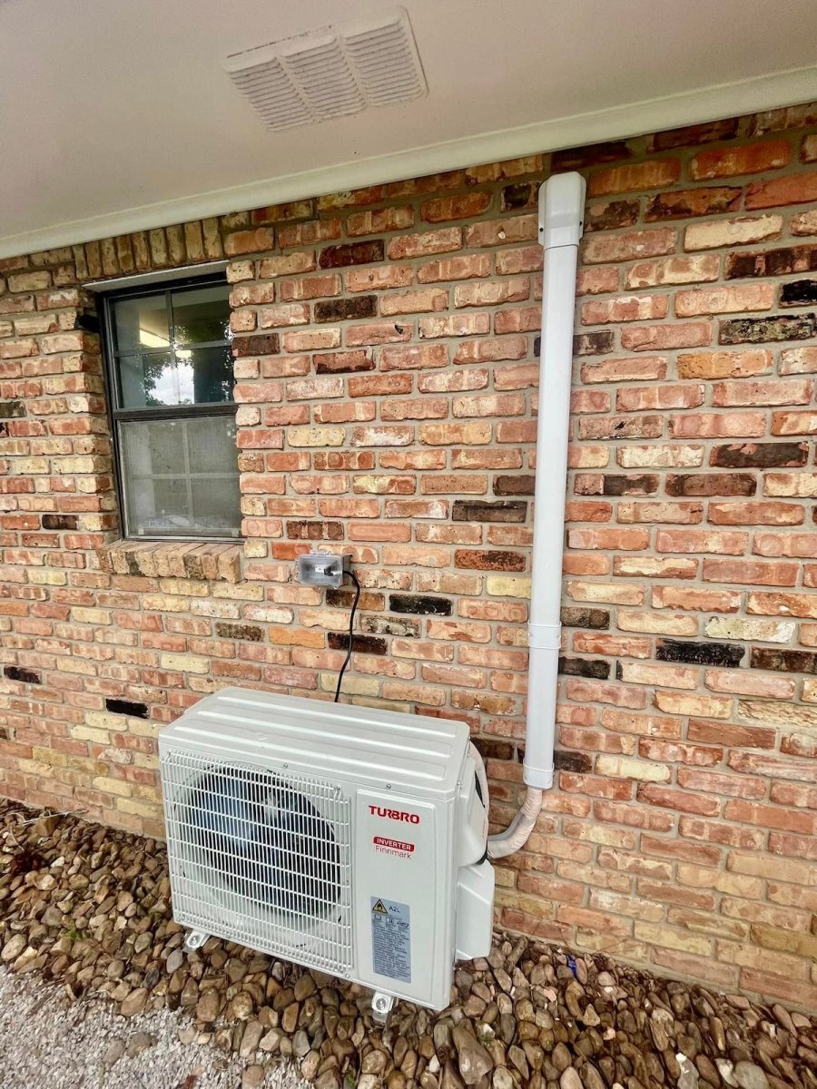 A Turbro heat pump installed on the exterior of a brick house.