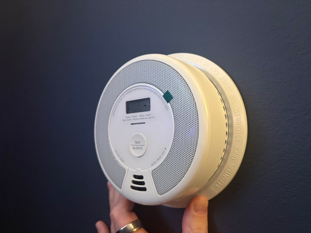 A product tester holding the X-Sense Smoke and CO alarm mount up against the wall before testing