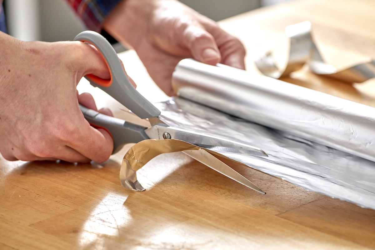 Woman uses scissors to cut through aluminum foil.