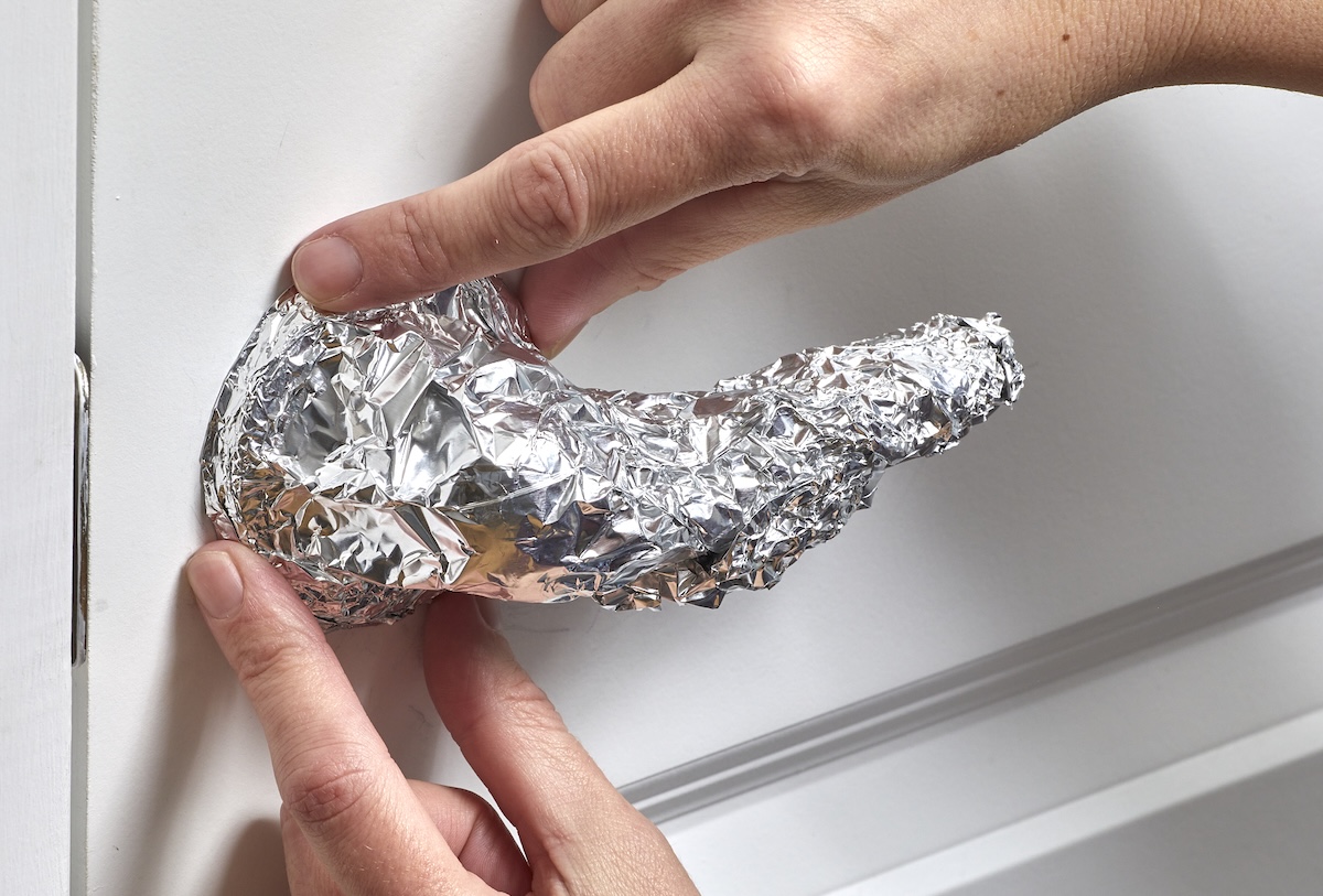 Woman positions aluminum foil wrapped around a lever door knob on an interior door.