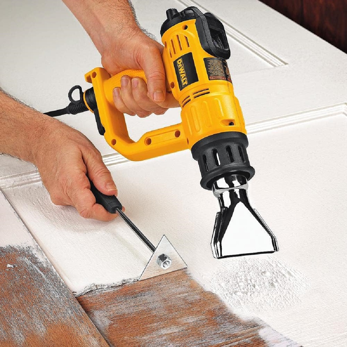 A person is using a heat gun to help remove paint with a scraper.