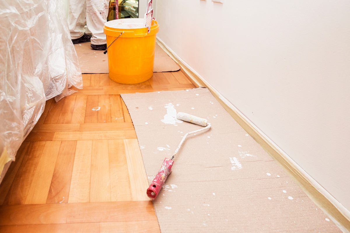 Paint roller lays on the brown paper protecting. a hardwood floor while room is being painted.