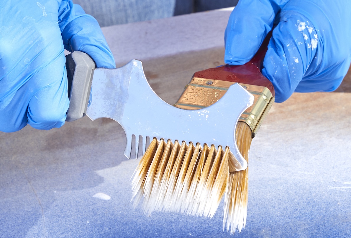 Person wearing nitrile gloves uses a painter's tool to comb paint brush bristles.