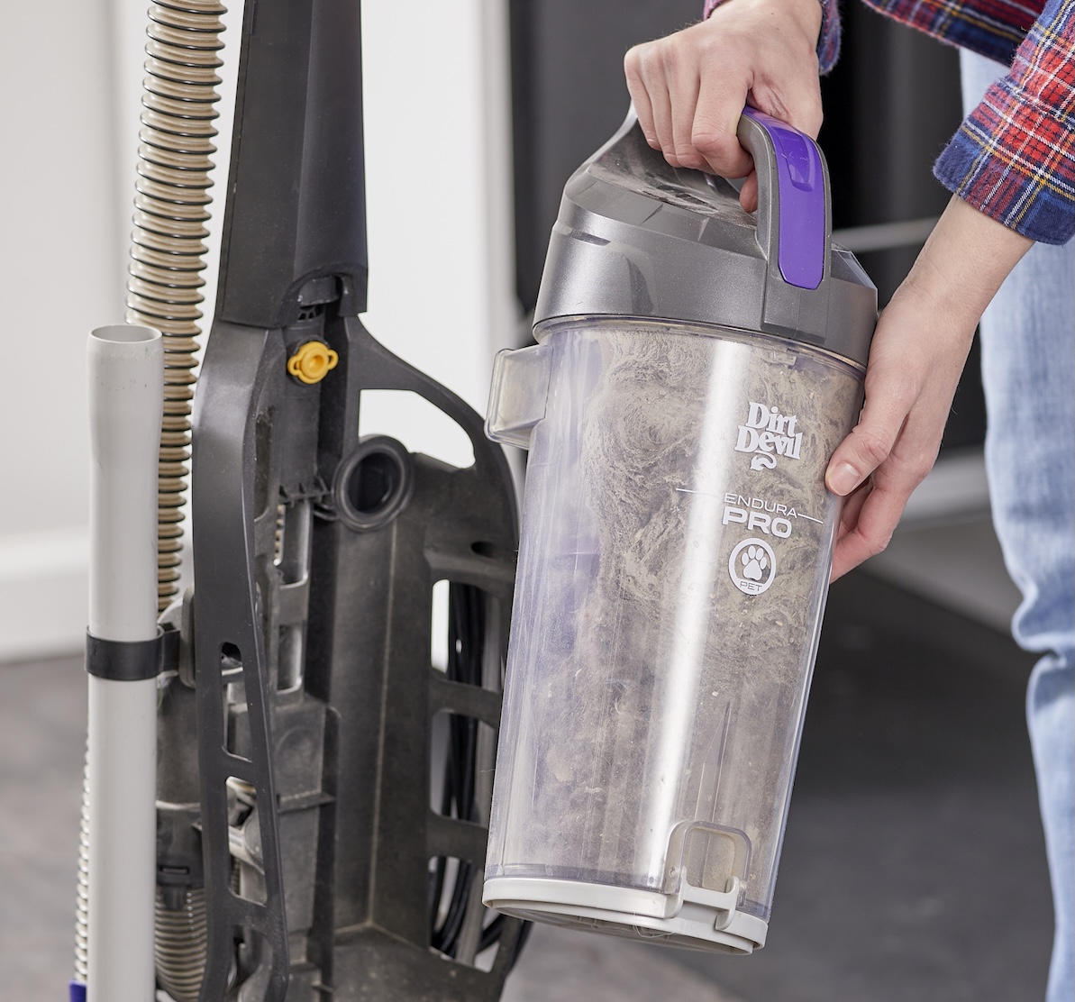 Woman removes dust canister from vacuum cleaner to empty it.