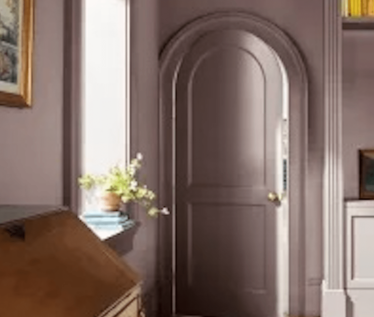 Benjamin Moore's Cinnamon Slate color-drenching an office with ornate trim work around a rounded door and a large window.