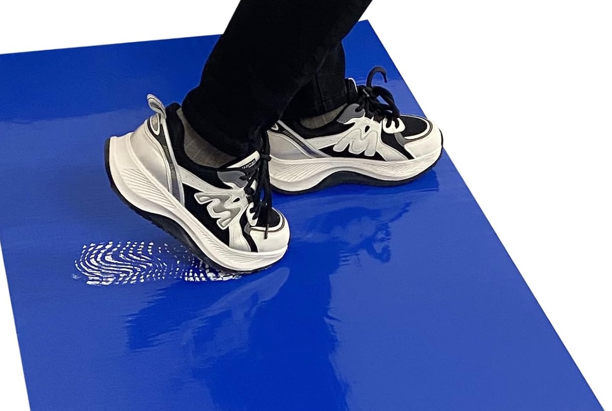 Person wearing black pants and sneakers tracks white paint on a blue floor sticky mat.