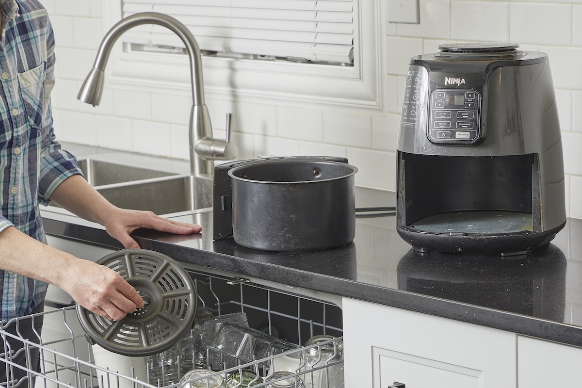 Woman dissembles an air fryer and puts washable parts in a dishwasher.