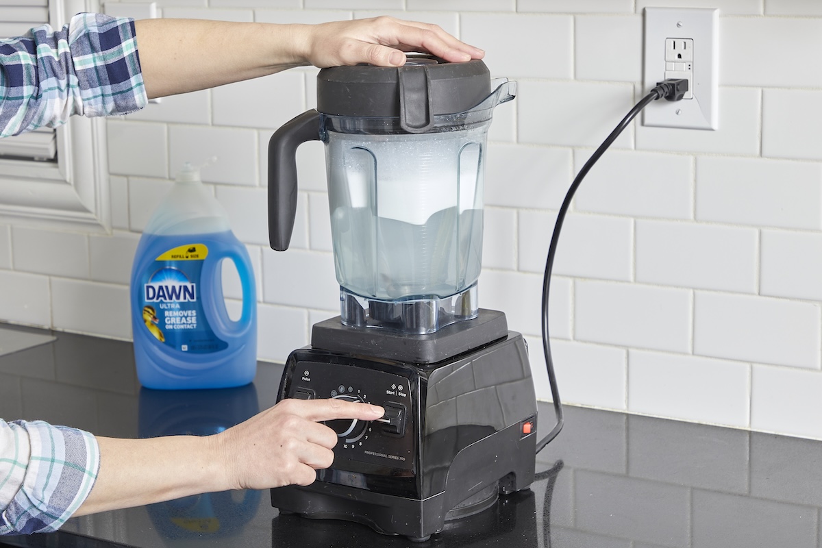 Woman cleans blender by blending dish soap and water and turning blender on.