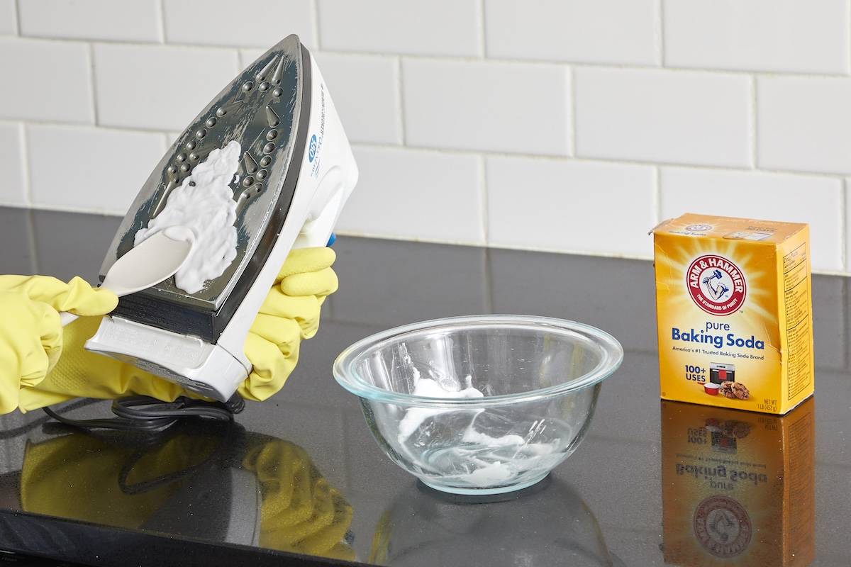 Woman applies a baking soda paste to the plate of an iron to clean it.