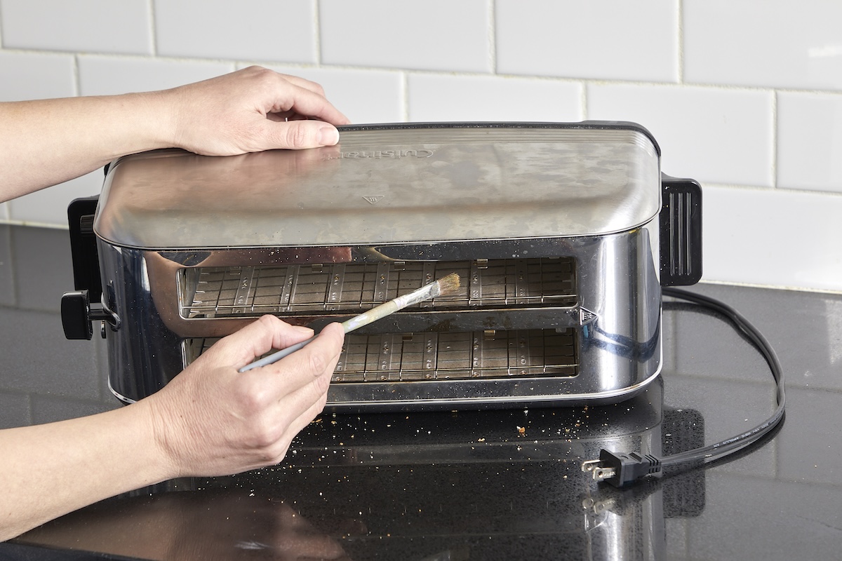 Woman uses a small brush to clean crumbs from the inside of a toaster.