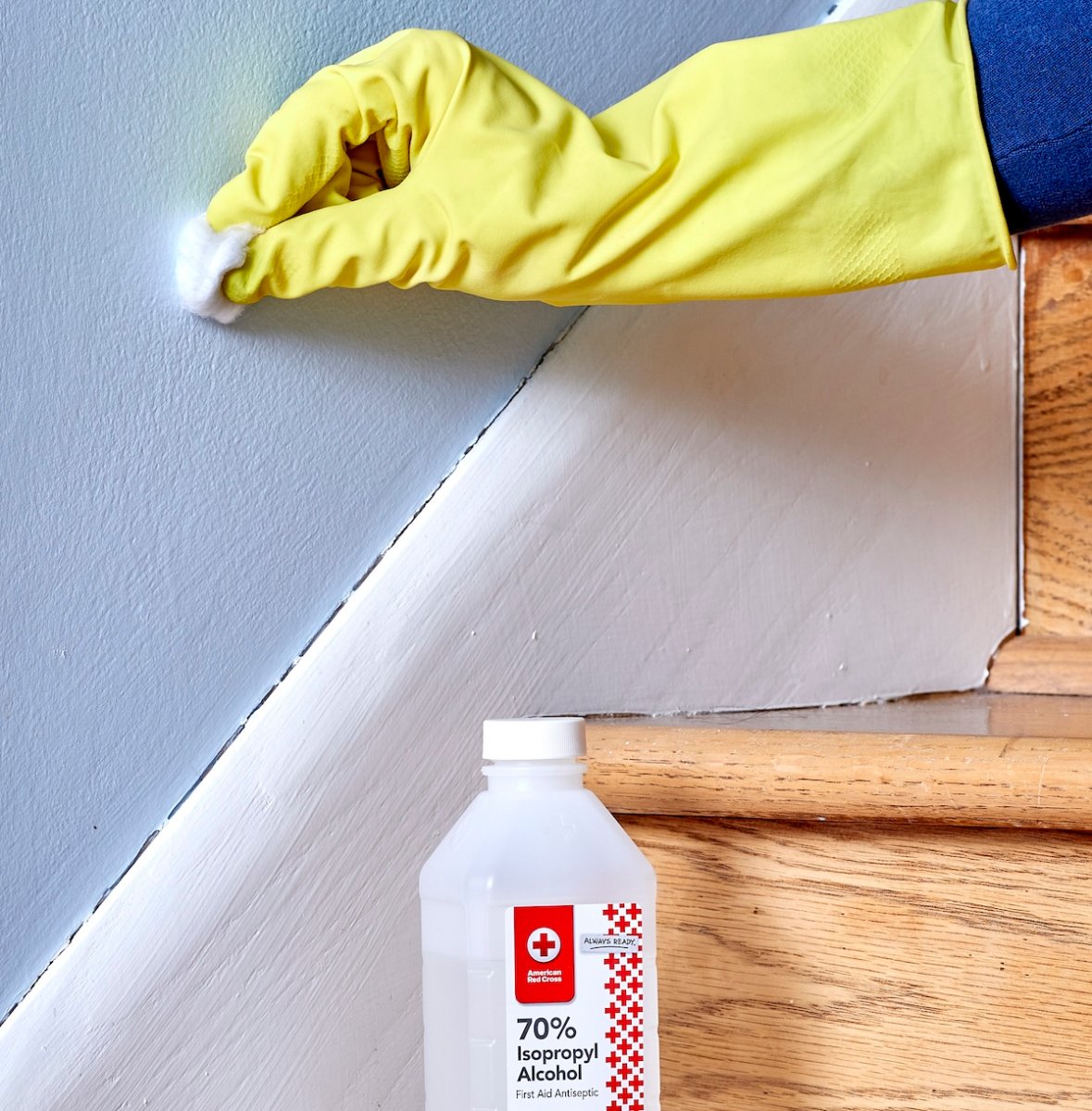 Woman wearing gloves rubs cotton ball dipped in isopropyl alcohol on a blue painted wall.
