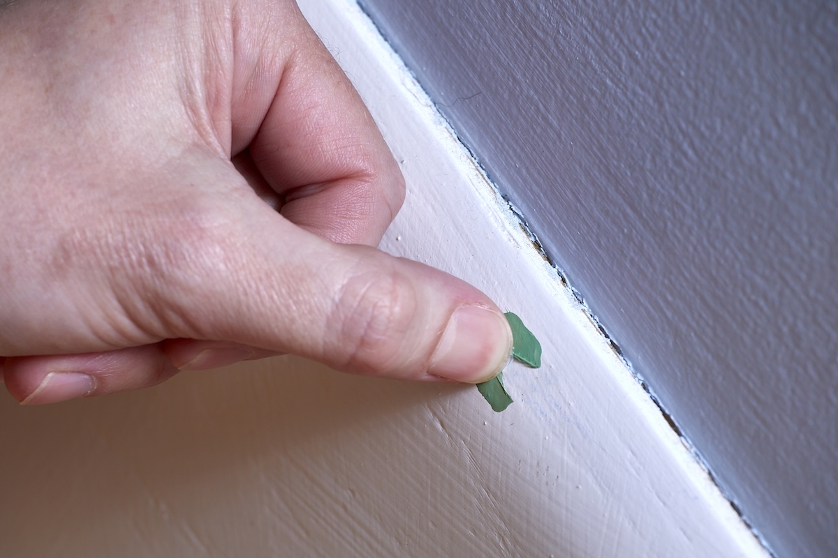 Woman scratches a dab of aqua paint that's on top of white painted indoor trim.