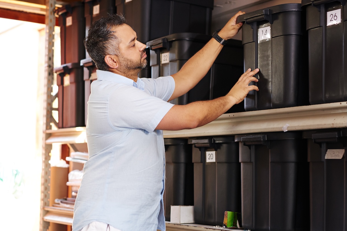 Man packing a large plastic black bin in the garage of his home for organization on shelves. 