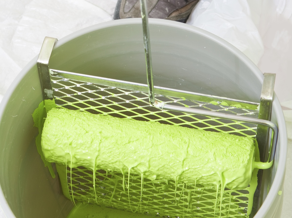 Paint roller dipped in neon chartreuse paint rolling against a paint screen in a bucket.