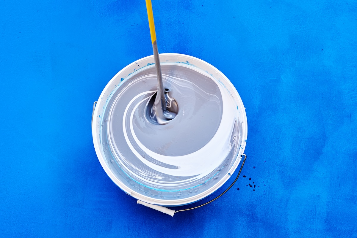 Tinting and mixing paint with stirring rod or mixer for paints, house painter added toner pigment to bucket, all on a blue background.