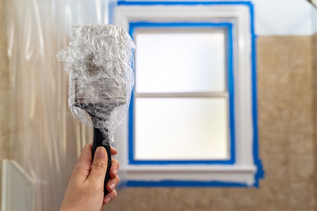 Woman's hand holds up a paintbrush wrapped in plastic wrap to protect the brush from drying out .