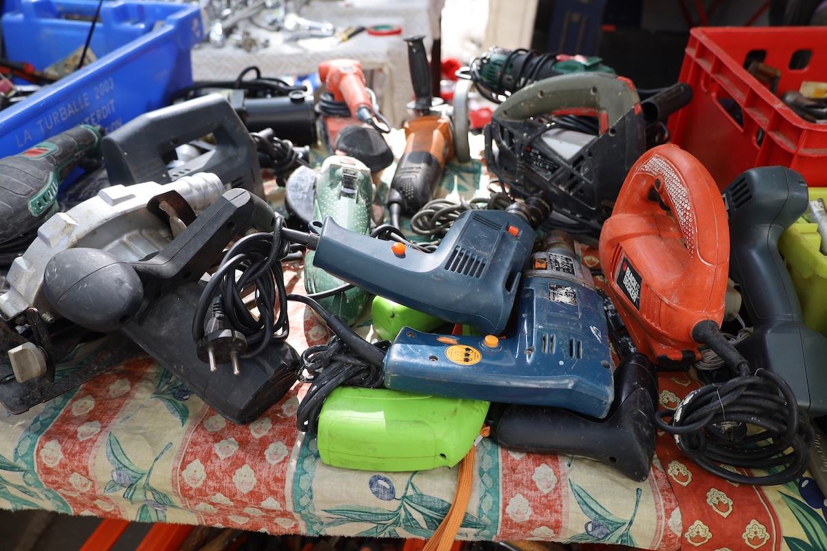 A table at a yard sale displays second-hand power tools.