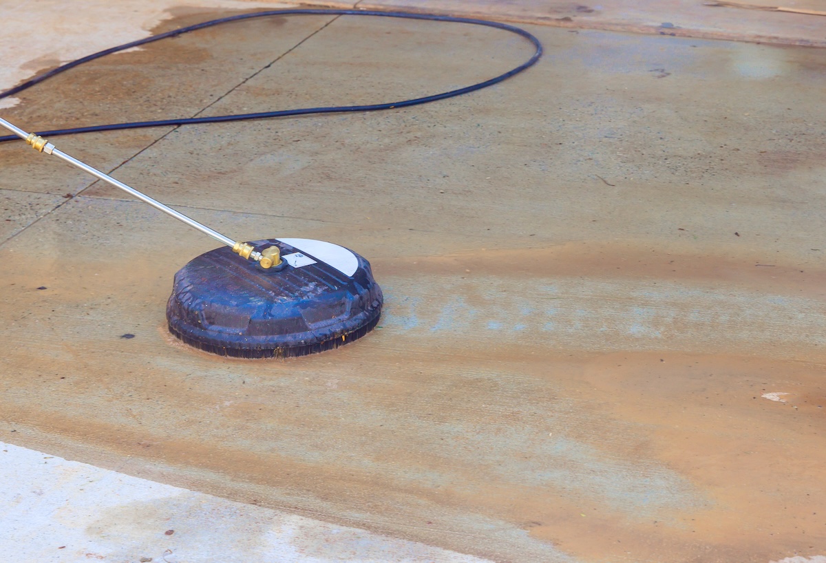 Person is pressure washing stained garage floor, spraying away water, on dirt.