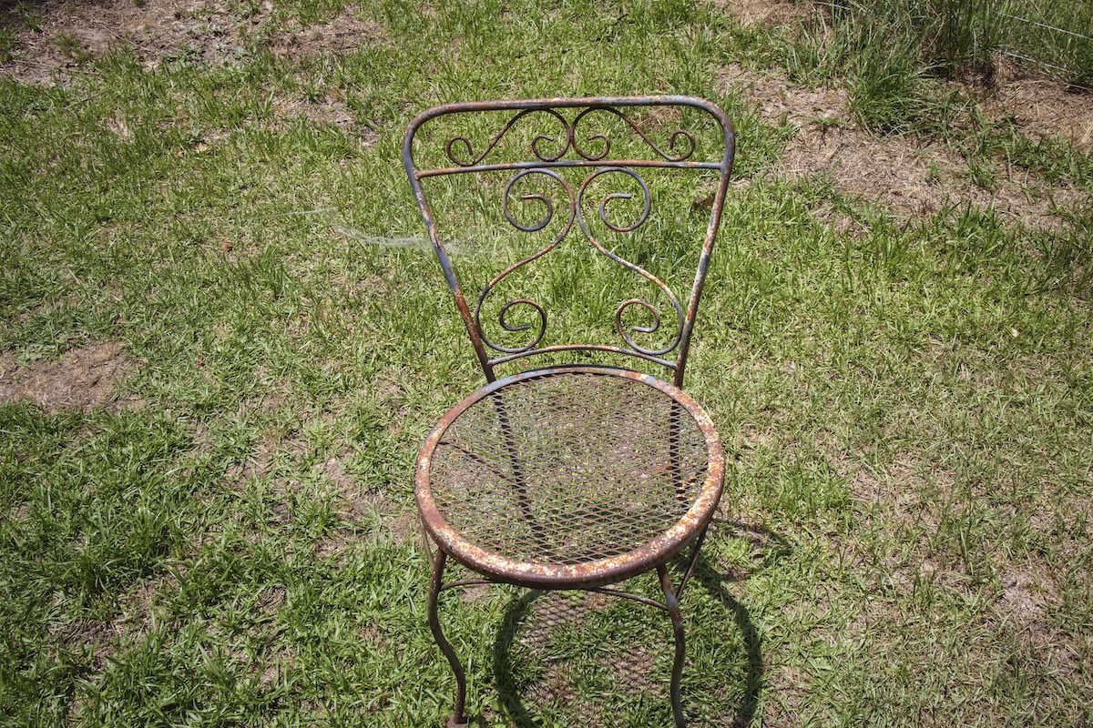 Old rusted vintage iron outdoor chair in patchy yard grass.