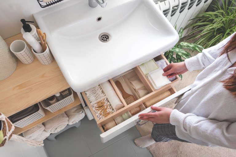 Top view of woman hands neatly organizing bathroom amenities and toiletries in drawer in bathroom.