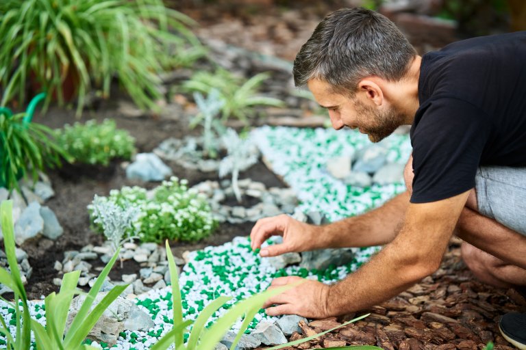 Man decorating flower beds in his garden with decorative gravel.