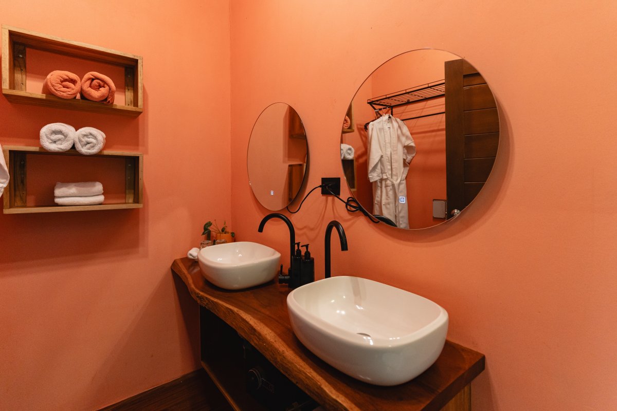 Bathroom with two round mirrors reflecting a bathrobe, clean towels, and terracotta colored walls