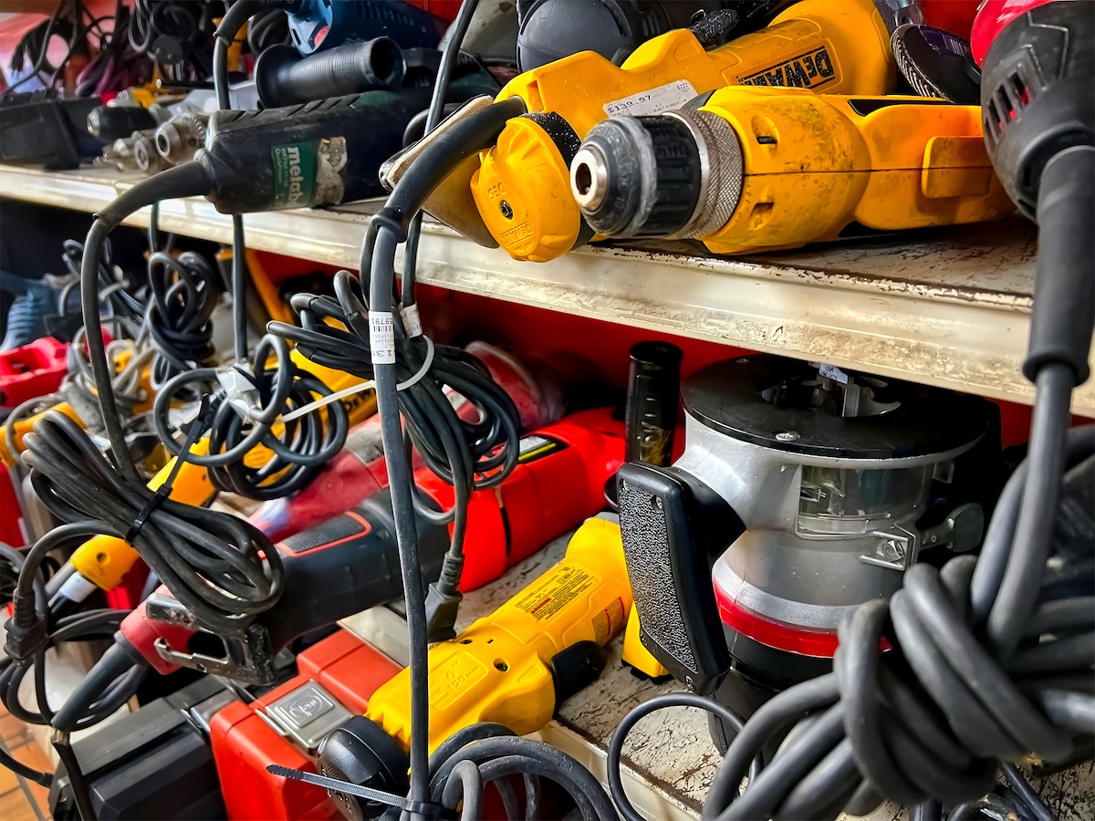 Several shelves at a second-hand store filled with used power tools of different brands. 