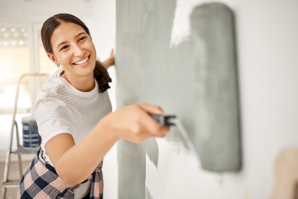 Young woman painting a home wall in a dusky blue, using a paint roller.