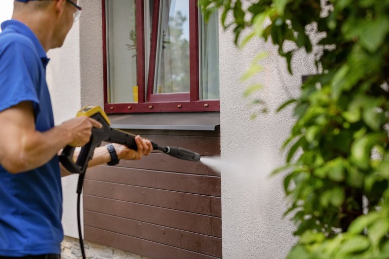 A homeowner washing the siding on his house with a power washer on low setting.
