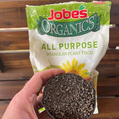 A person holding a cup of Jobe's All Purpose fertilizer in front of its bag before testing