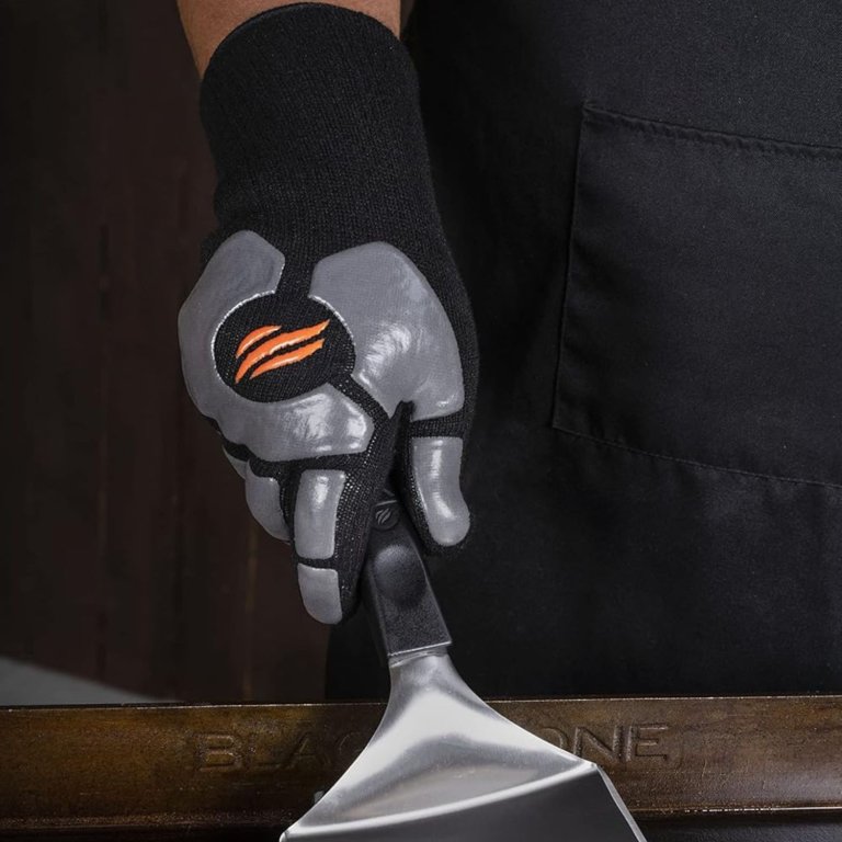 A person wearing the Blackstone Grill and Griddle Gloves while holding a spatula