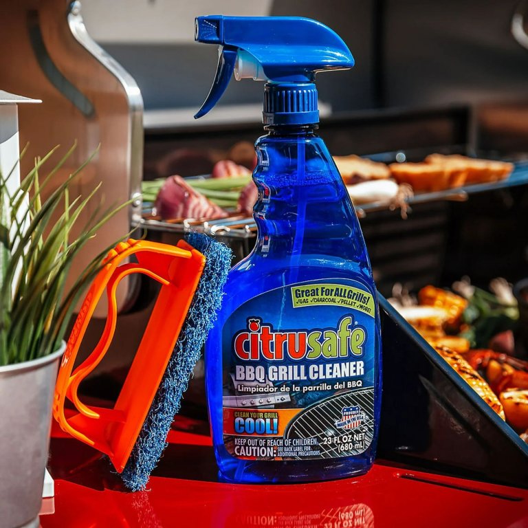 The CitruSafe BBQ Grill Cleaner next to a scrub brush with a grill full of food in the background