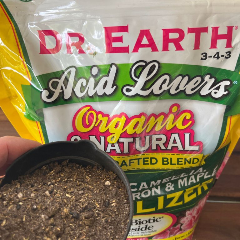 A person holding a cup of the Dr. Earth Organic and Natural Acid Lovers Fertilizer in front of its bag before testing