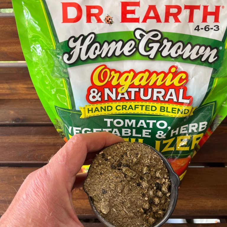 A person holding a cup of Dr. Earth Organic and Natural Home Grown Fertilizer in front of its bag before testing