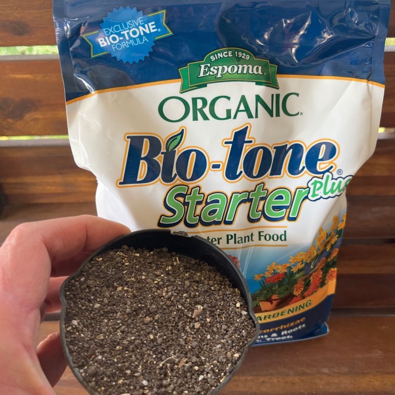 A person holding a cup of the Espoma Organic Bio-tone Starter Plus Fertilizer in front of its bag before testing