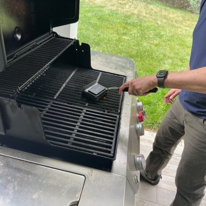 A product tester using the GrillArt SteamWizards Steam-Cleaning Grill Brush to clean grill grates