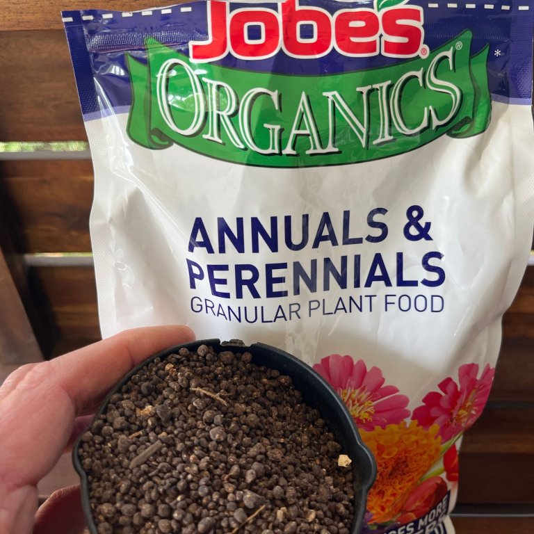 A person holding a cup of Jobe’s Organics Annuals and Perennials Plant Food in front of its bag before testing